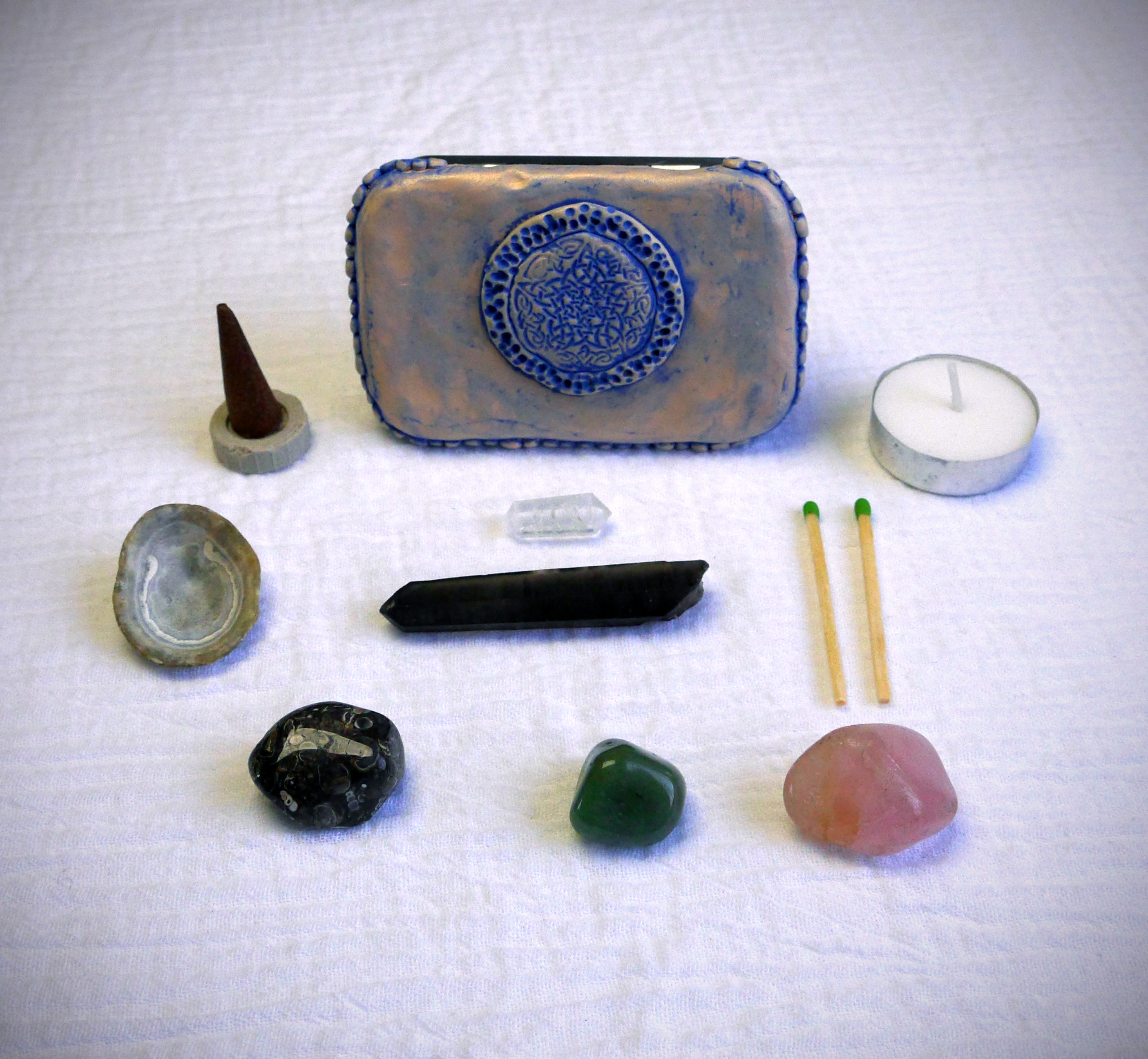 Altoids tin travel altar decorated with polymer clay, with crystals, incense, tea light candles, an offering shell, and matches