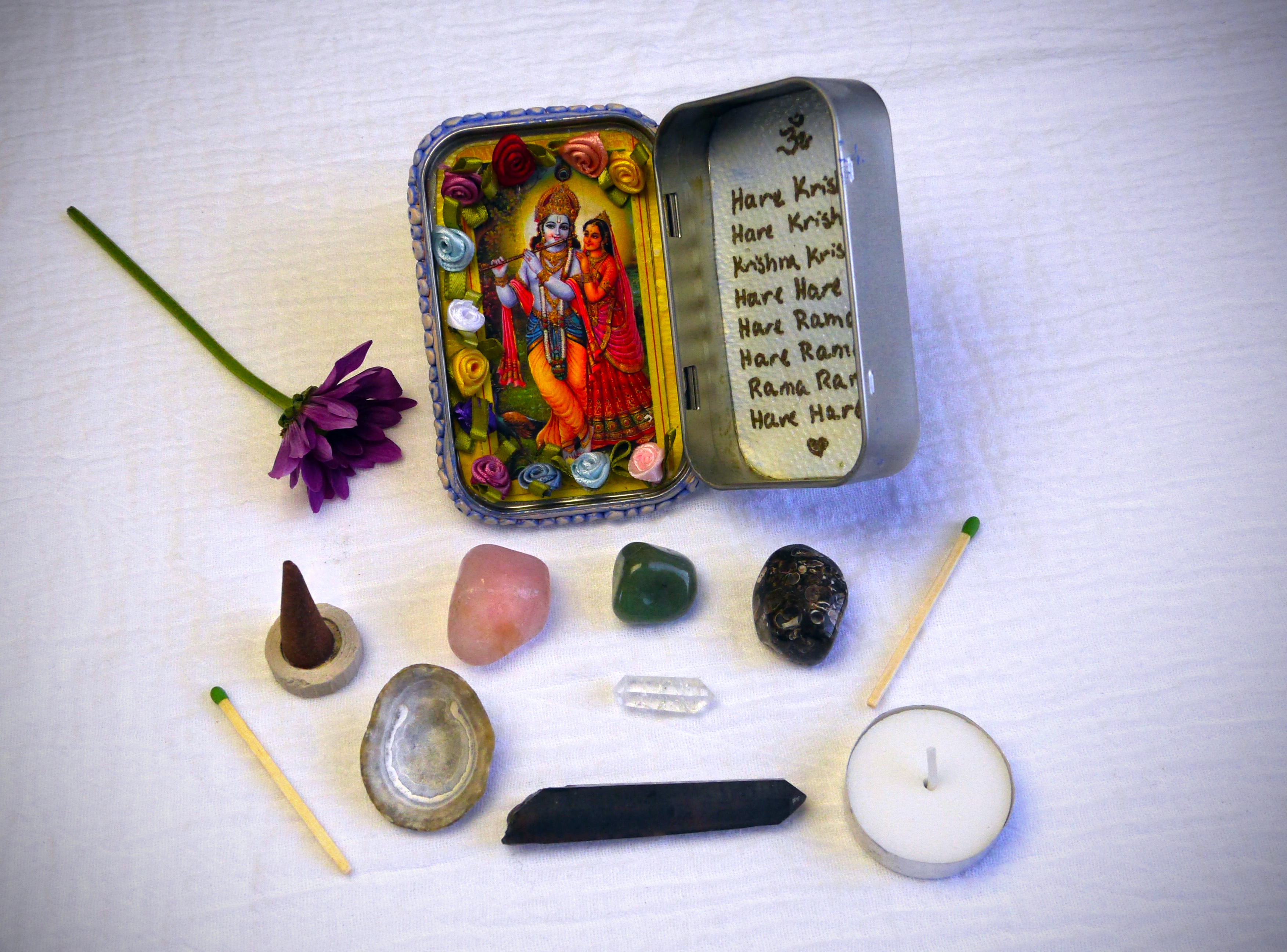 Travel altar with Sri Sri Radha Krishna, mantra, crystals, incense, a tea light candle, and a tiny wand.