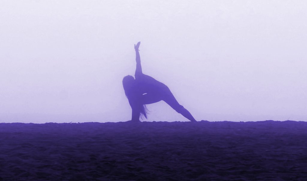 Purple silhouette of a girl doing yoga Side Angle Pose on a foggy beach.