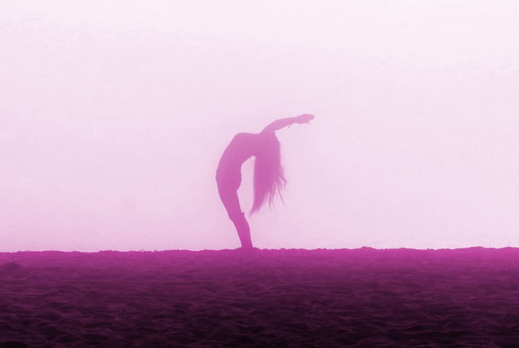Hot pink silhouette of a girl doing yoga Backbend on a foggy beach.