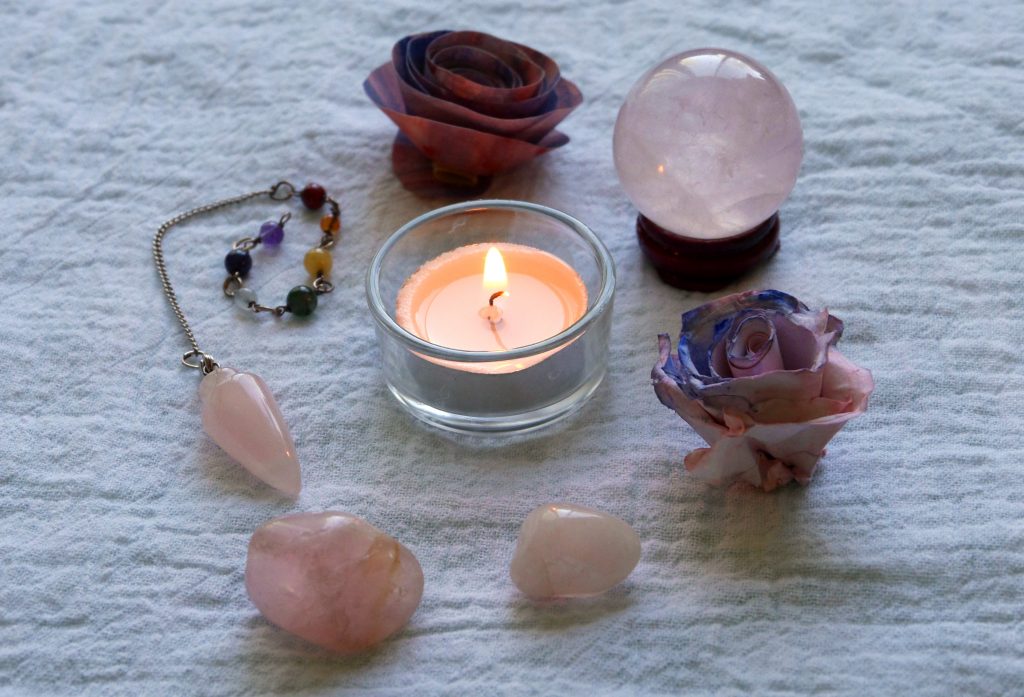 Rose quartz tumbled stones, rose quartz pendulum, rose quartz crystal ball, candle.