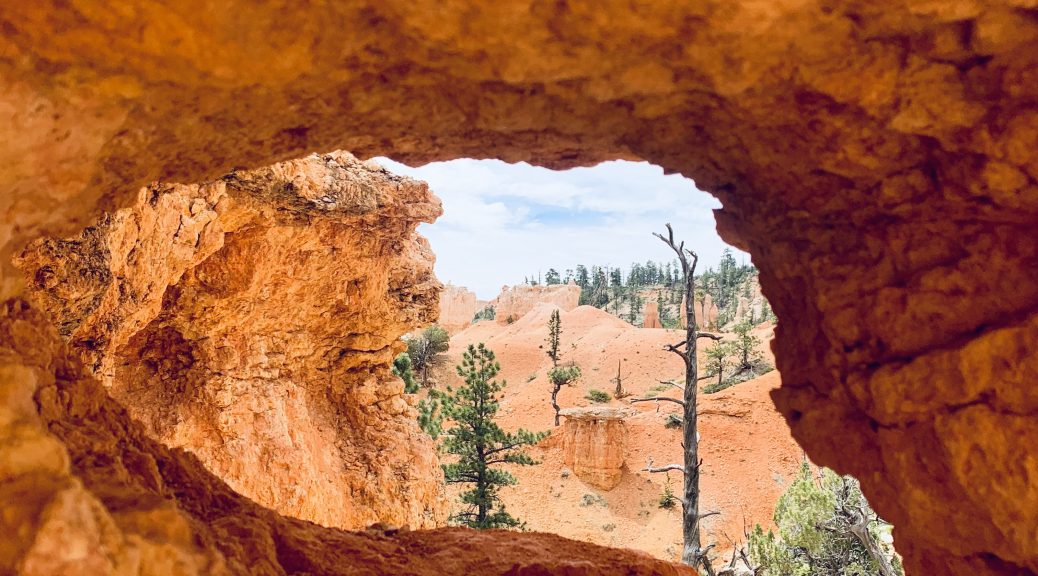Looking through a large hole in red-orange rocks to a surreal, desert canyon landscape.
