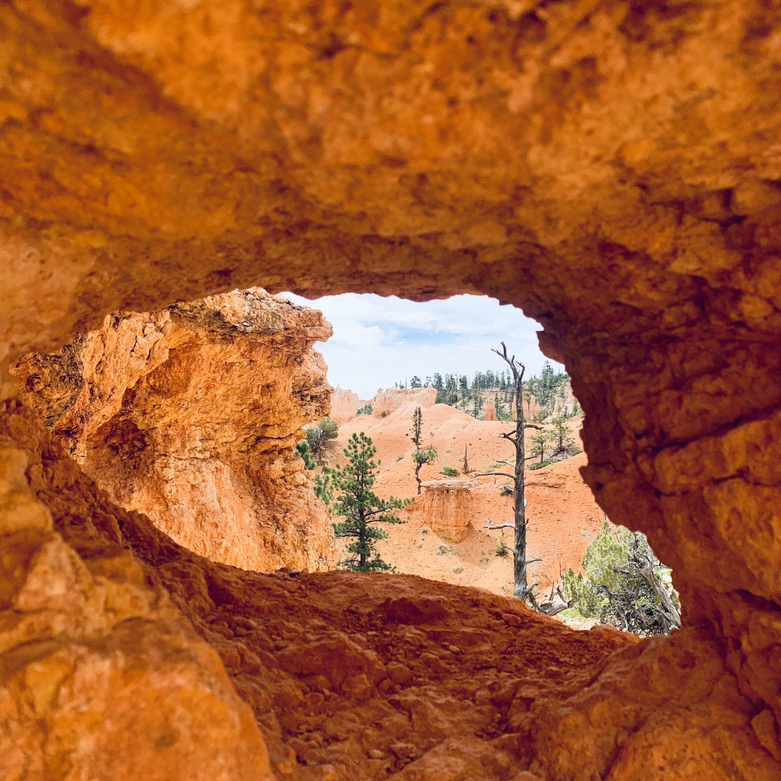 Looking through a large hole in red-orange rocks to a surreal, desert canyon landscape.